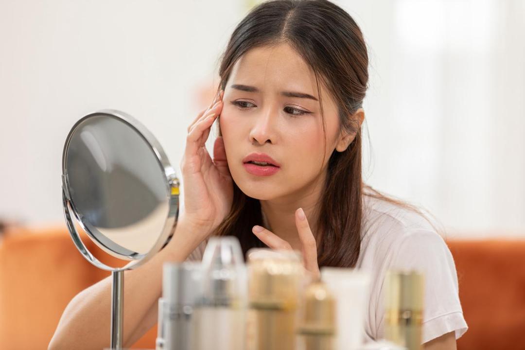 Seorang perempuan sedang skincare-an dan melihat ke cermin.