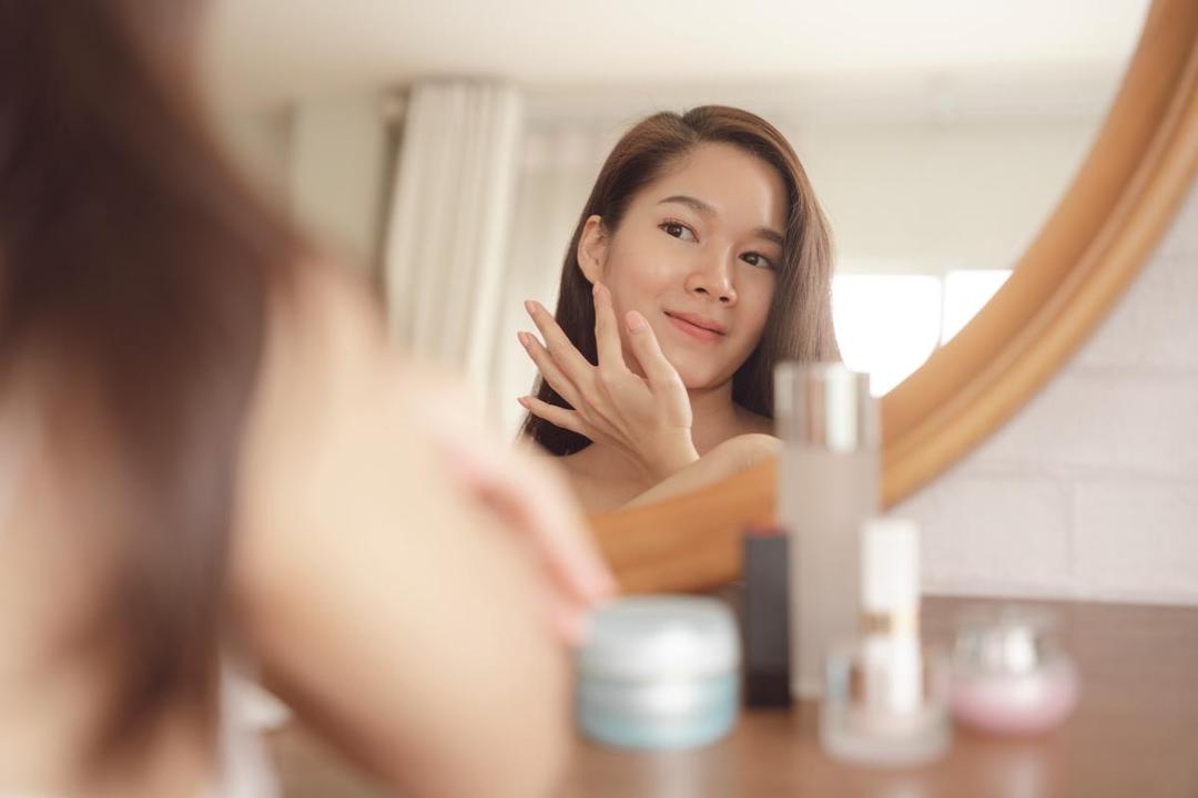 Seorang perempuan sedang skincare-an dan melihat ke cermin.