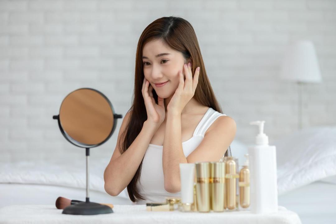Seorang perempuan sedang skincare-an dan melihat ke cermin.