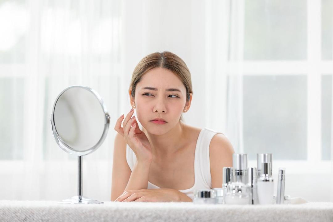 Seorang perempuan sedang skincare-an dan melihat ke cermin.