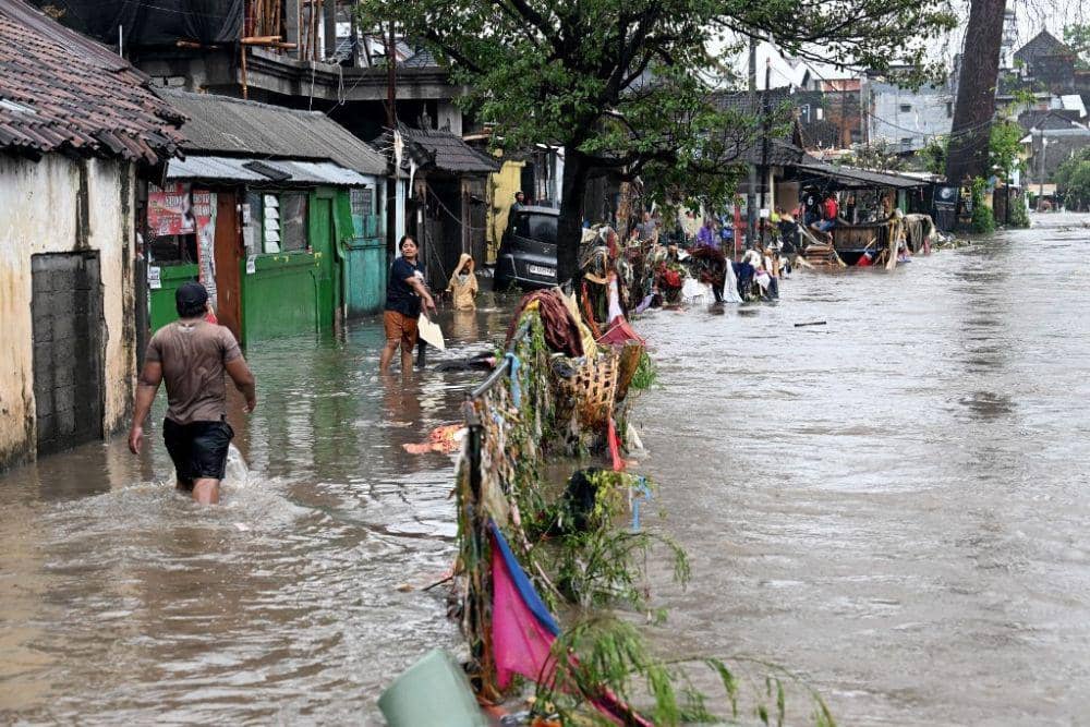 Warga menerjang banjir di permukiman mereka usai hujan lebat mengguyur Denpasar, Bali, Rabu (10/9/2025). (AFP/Sonny Tumbelaka via thejakartapost.com)