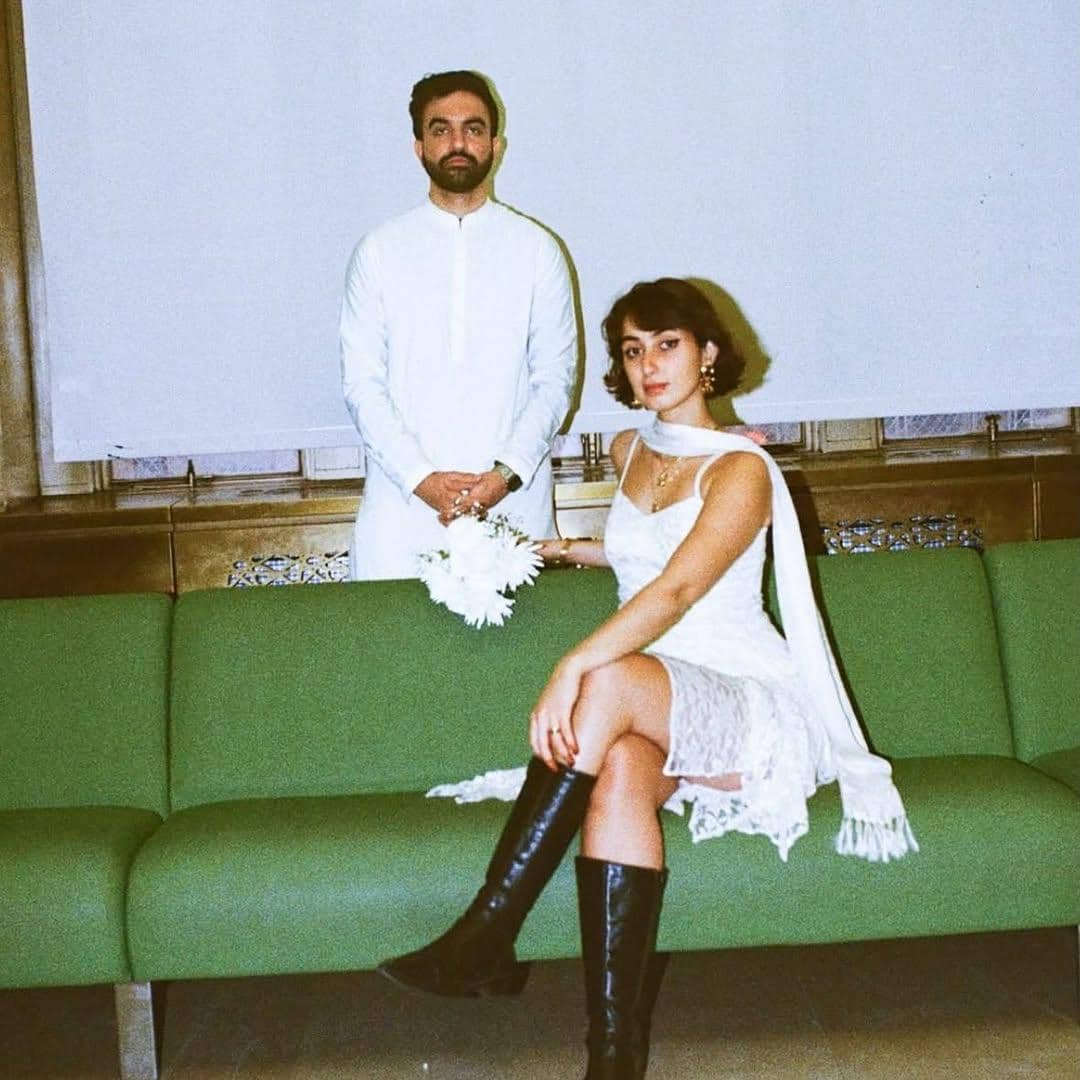 Rama Duwaji bergaya chic sekaligus edgy dengan lace dress putih dipadukan scarf panjang dan boots hitam.