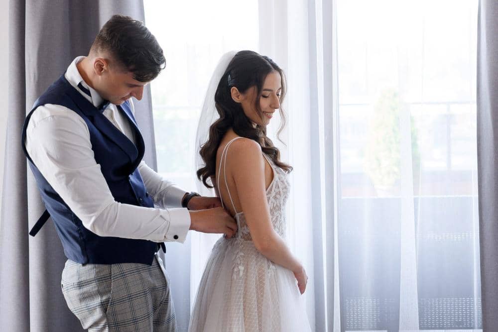 attractive-man-groom-helps-bride-with-wedding-dress-standing-brides-couple-preparing-wedding-ceremony-together-spacious-apartment-front-large-window.jpg