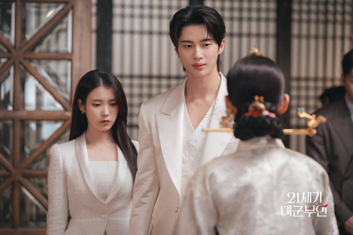 Dua pemeran drama Korea Perfect Crown mengenakan busana putih elegan berdiri di hadapan wanita berkimono tradisional di ruangan bergaya klasik.