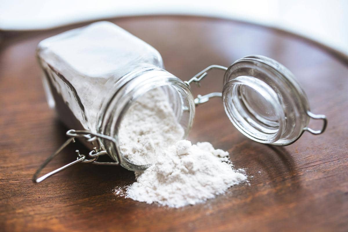 Ilustrasi baking soda tumpah dari toples kaca di atas meja kayu