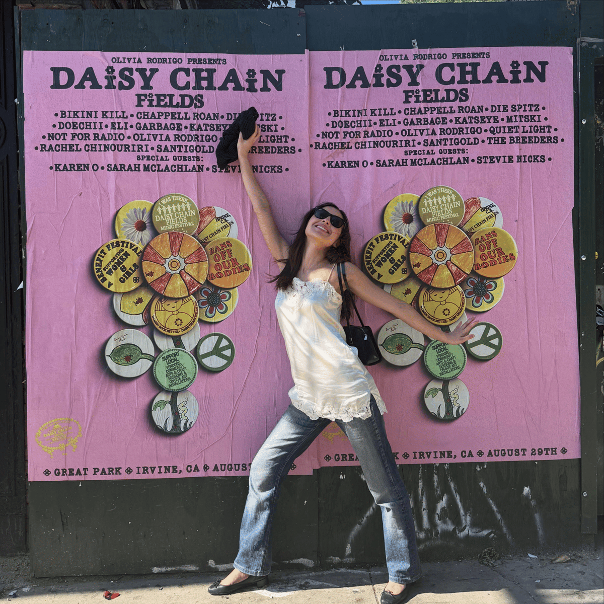 Olivia Rodrigo berpose ceria di depan poster festival musik Daisy Chain Fields berwarna pink dengan daftar artis yang akan tampil.