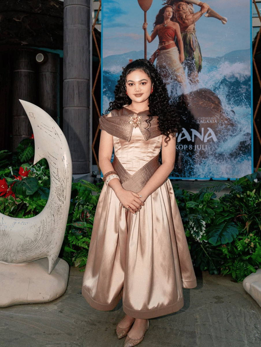 Amora Lemos mengenakan gaun satin berwarna emas muda berpose di depan poster film Moana Live Action di Plaza Senayan.