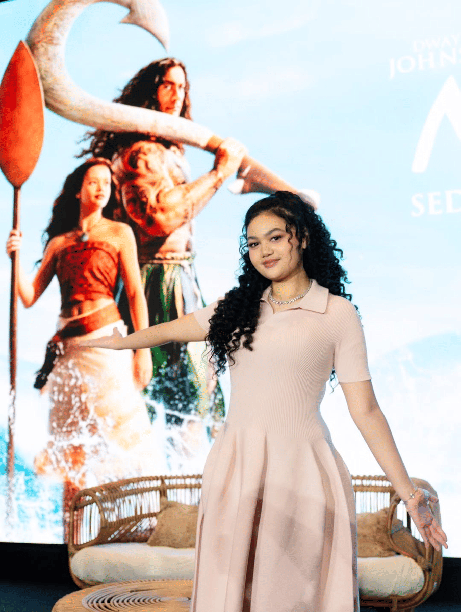Amora Lemos yang bergaun krem berpose di depan layar besar bergambar karakter film Moana Live Action di Plaza Senayan.