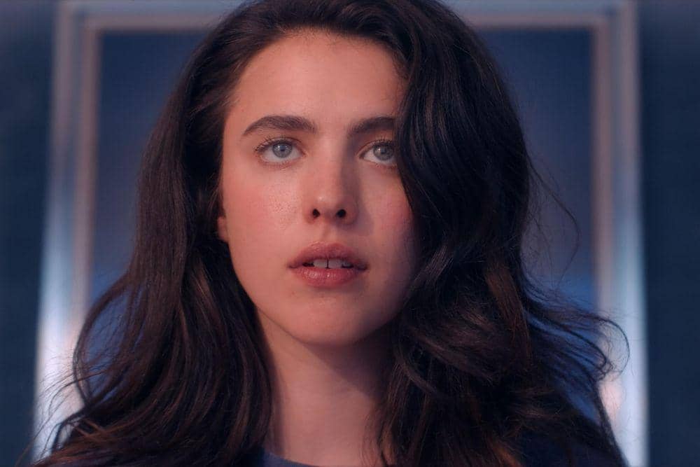 Margaret Qualley yang berambut panjang bergelombang menatap lurus ke depan dengan ekspresi serius dalam pencahayaan lembut bernuansa biru.