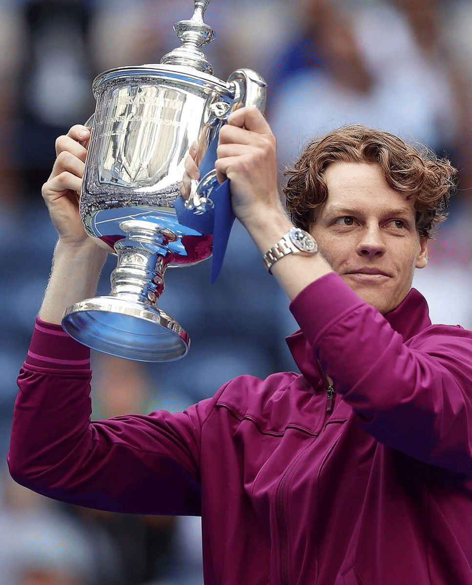 Jannik Sinner mengenakan jaket ungu mengangkat trofi besar perak setelah memenangkan turnamen tenis US Open 2024.