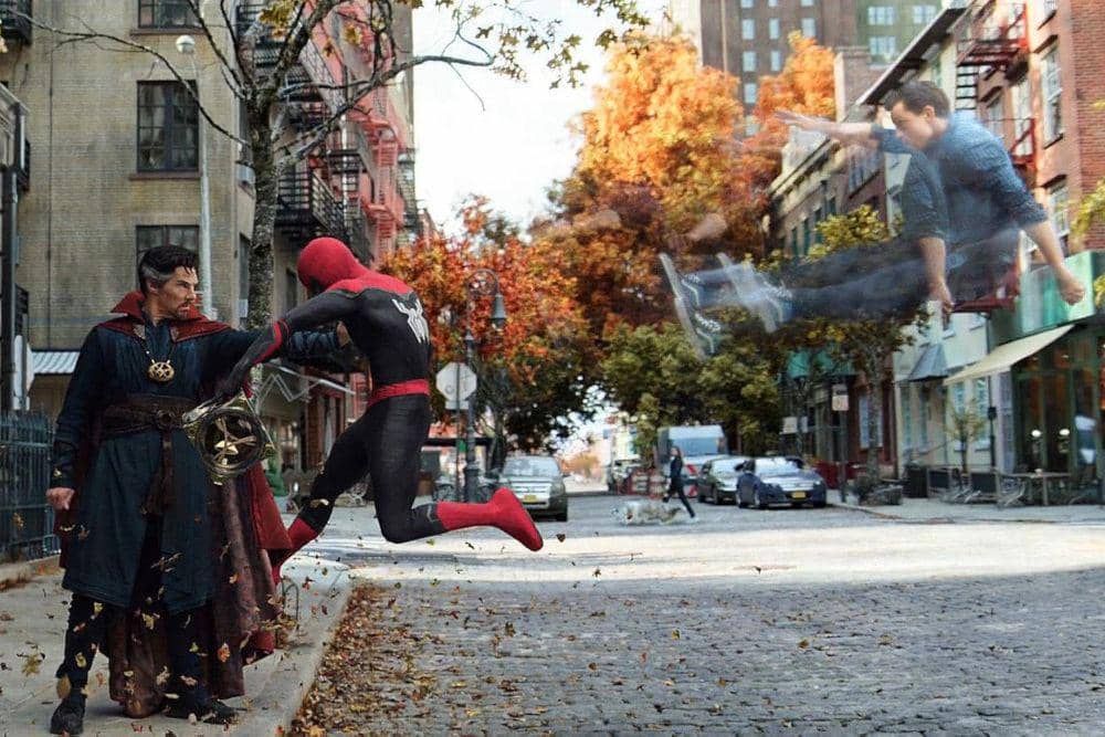 Dua karakter dari film Spider-Man: No Way Home tampak bertarung di jalan kota dengan latar pepohonan musim gugur dan gedung bertingkat.