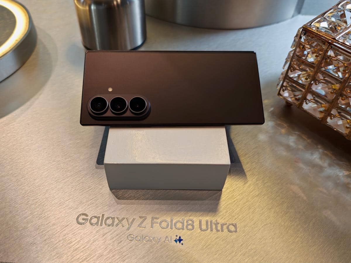 Tampak belakang Samsung Galaxy Z Fold8 Ultra berwarna gelap dengan tiga kamera utama, diletakkan di atas meja logam elegan.