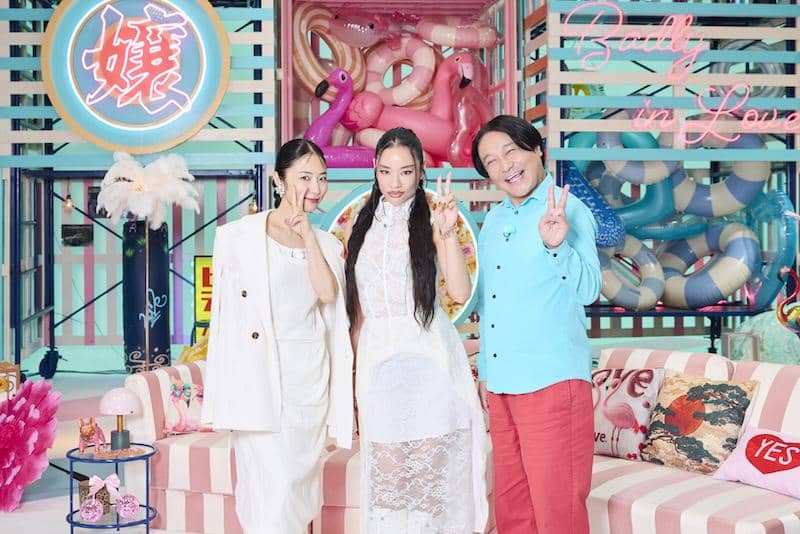 Tiga pembawa acara berdiri di set berwarna pastel dengan dekorasi flamingo dan pelampung, mempromosikan Badly in Love: Season 2.