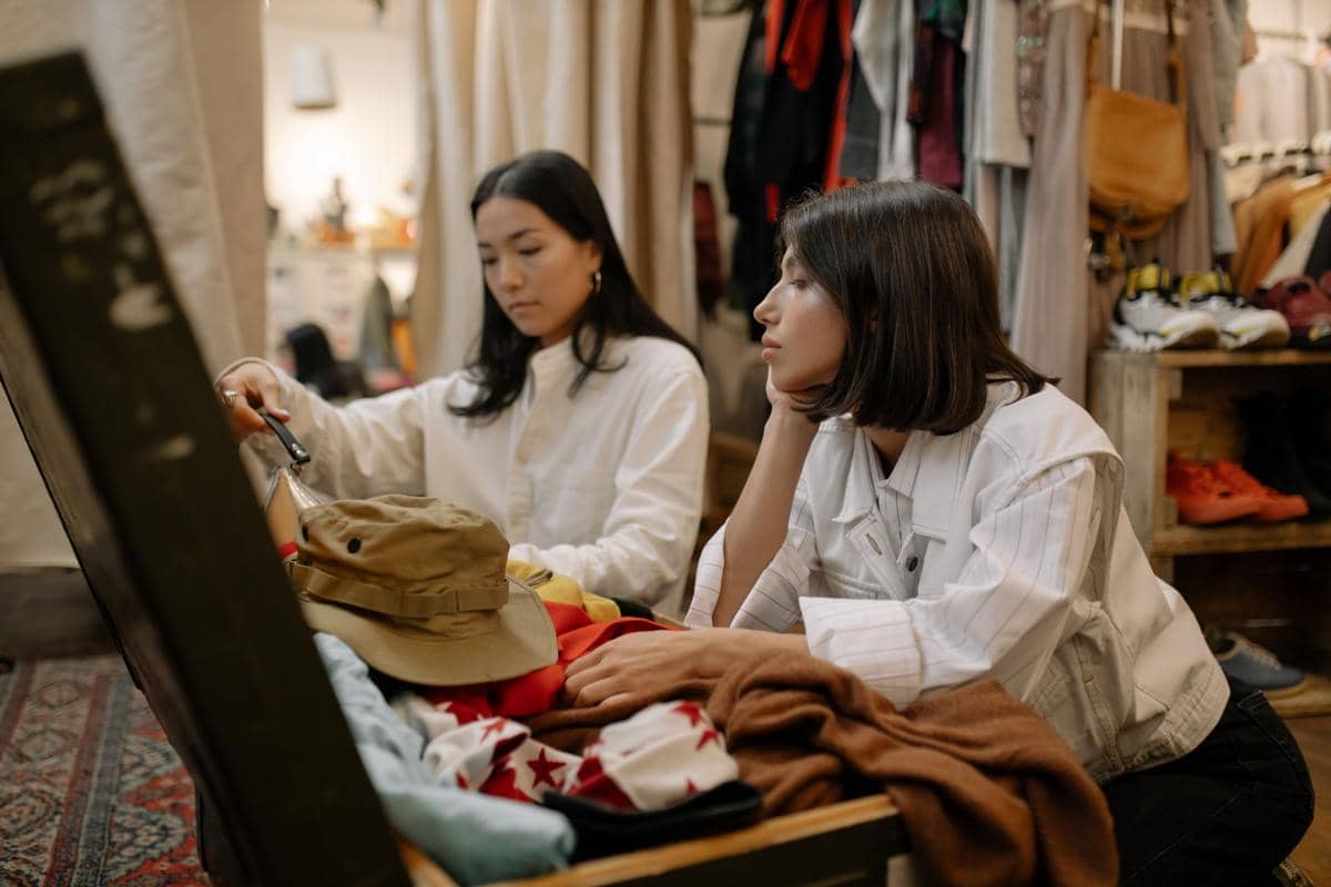 Dua perempuan memilih pakaian di thrift shop.