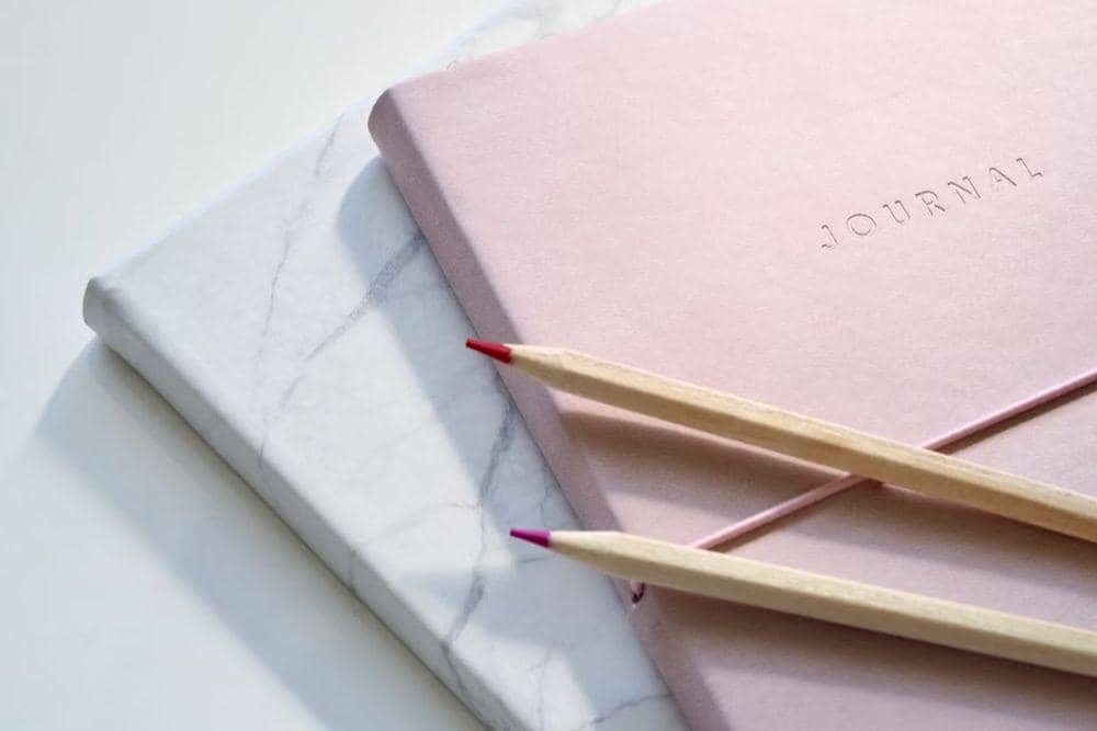 Notebook travel journal terbuka dengan perlengkapan tulis dan dekorasi di atas meja sebagai ilustrasi catatan perjalanan.